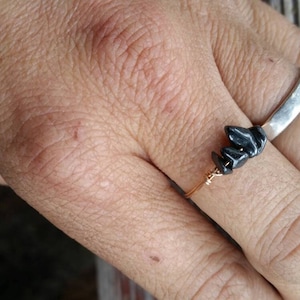 Puede incluir: Un anillo de plata con un acento de piedra negra. El anillo se lleva en el dedo de una persona.