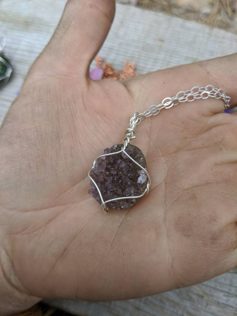 May include: A silver chain necklace with a purple amethyst crystal pendant wrapped in silver wire.