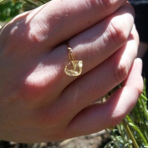 May include: A gold ring with a clear yellow gemstone. The ring is on a person's finger.