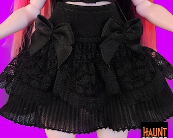 May include: Black doll skirt with two bows and a lace trim. The skirt is part of a doll outfit. The image includes the text "HAUNT COUTURE" in a black box.