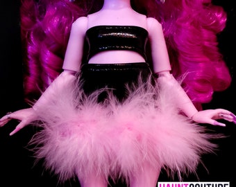 Puede incluir: Una muñeca con cabello rosa brillante, con un top y una falda negros. La falda está adornada con plumas rosas. La muñeca lleva pendientes plateados y uñas largas y moradas. El texto "HAUNT COUTURE" es visible en la esquina inferior derecha.