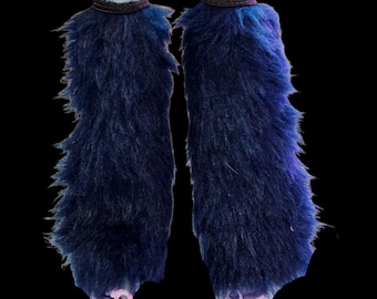 May include: Two blue faux fur leg warmers with a dark band at the top. The leg warmers are a deep blue color with a shaggy texture. The background is black.