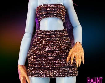 May include: A black and gold glittery crop top and mini skirt set. The skirt has a high waist and the top is strapless. The set is made of a stretchy fabric and has a sparkly finish.