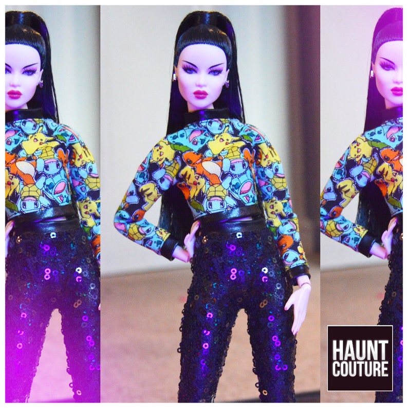 Pu&ograve; includere: Una bambola di moda che indossa un top corto nero e blu con una stampa Pokemon e pantaloni neri di paillettes. La bambola ha lunghi capelli neri e indossa un choker nero. Lo sfondo &egrave; un gradiente viola e rosa. Il testo "HAUNT COUTURE" &egrave; visibile nell'angolo in basso a destra dell'immagine.