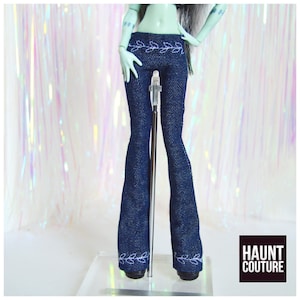 May include: Dark blue denim doll pants with a flared leg design. The pants feature white embroidered leaf patterns along the waistband and the bottom hem. The Haunt Couture logo is in the bottom right corner.