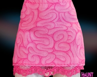 Puede incluir: Minifalda rosa brillante con un patrón similar a un cerebro. La falda tiene un ribete de encaje en el dobladillo y el texto "HAUNT COUTURE" en fuente morada y blanca.