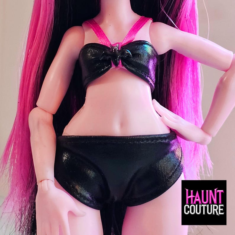 K&ouml;nnte beinhalten: Schwarzer und pinkfarbener zweiteiliger Badeanzug mit einem Fledermaus-Design auf dem Oberteil. Der Badeanzug ist aus gl&auml;nzendem Stoff. Der Text "HAUNT COUTURE" ist in der rechten unteren Ecke des Bildes sichtbar.