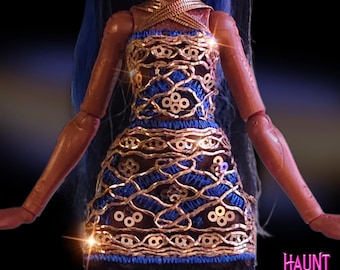 May include: A doll wearing a blue and gold dress with a black lace hem. The dress features a gold lattice design over a blue fabric, with gold embellishments. The doll has blue hair and the text "HAUNT COUTURE" is visible in the lower right corner.