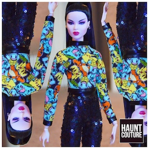 May include: A fashion doll wearing a black and blue sequined outfit with a colorful crop top featuring a pattern of cartoon characters. The doll has long black hair and red lipstick. The text "HAUNT COUTURE" is visible in the bottom right corner of the image.