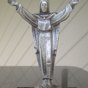 May include: A silver statue of Jesus Christ with outstretched arms, standing on a black base.