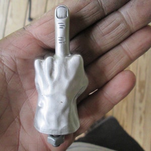 Könnte beinhalten: Eine silberne Metallskulptur einer Hand, die den Mittelfinger zeigt.