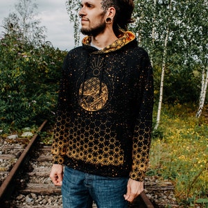 May include: A black hoodie with a gold geometric pattern and a graphic of a mountain range and a sun. The hoodie has a drawstring hood and a kangaroo pocket.