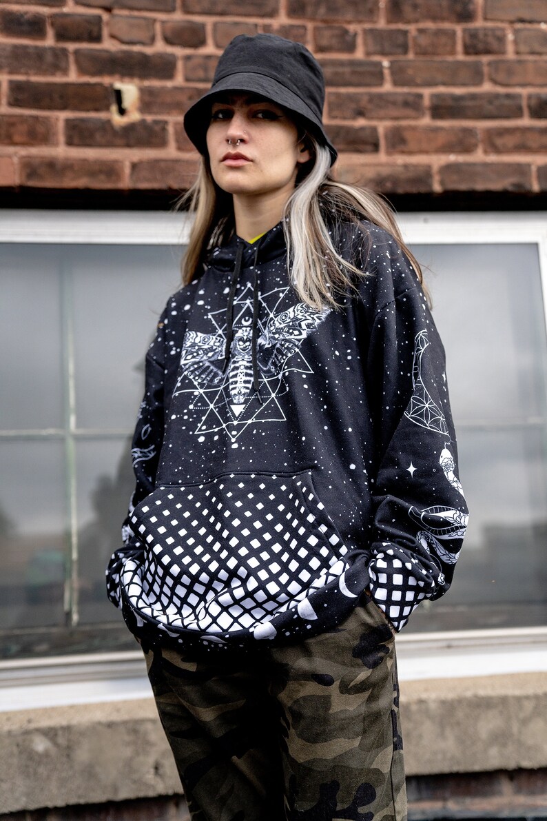 Peut inclure: Un sweat-shirt noir avec un motif blanc imprim&eacute; d'un papillon de nuit, de formes g&eacute;om&eacute;triques et d'&eacute;toiles. Le sweat-shirt a un motif &agrave; carreaux noir et blanc sur la moiti&eacute; inf&eacute;rieure. Le mod&egrave;le porte un chapeau noir en forme de seau.