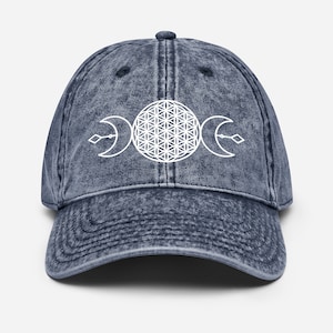 May include: A blue denim baseball cap with a white flower of life and triple moon symbol.