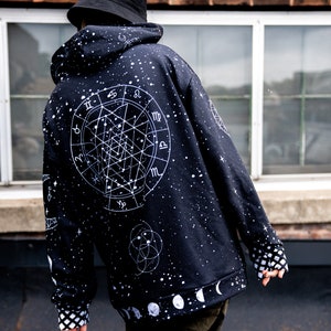 Peut inclure: Sweat-shirt noir avec un imprim&eacute; de constellation et de zodiaque blanc. Le sweat-shirt a une capuche avec cordon de serrage et un imprim&eacute; de phases de lune blanc sur l'ourlet inf&eacute;rieur.