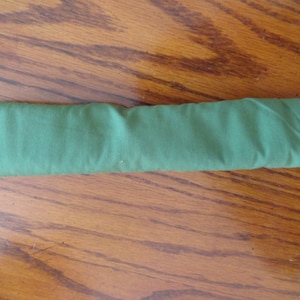 May include: A folded, rectangular green fabric item, possibly a cloth or accessory. The fabric has a slightly textured appearance and is neatly folded, suggesting it's a new or unused item. The color is a solid, medium green.