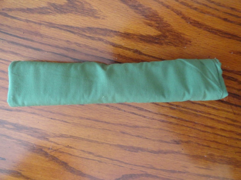 May include: A folded, rectangular green fabric item, possibly a cloth or accessory. The fabric has a slightly textured appearance and is neatly folded, suggesting it's a new or unused item. The color is a solid, medium green.