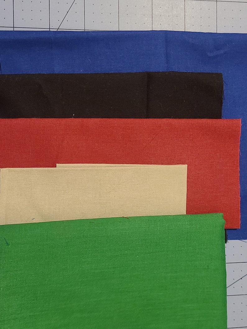 May include: A collection of fabric swatches in various colors, including blue, black, red, beige, and green. The fabric pieces are rectangular and arranged in a layered composition, showcasing the different hues and textures.