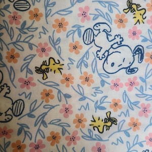 Pode incluir: Tecido branco com um padrão repetido de cães de desenho animado azuis e amarelos, flores rosa e laranja e folhas azuis.