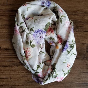 May include: White floral print infinity scarf with a variety of pink, purple, and green flowers.