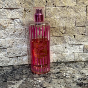 May include: A clear glass perfume bottle with pink vertical stripes and a pink cap. The bottle contains a pink liquid and has the words "Pink Candy Pour Femme" printed on the front.