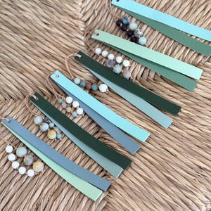 May include: A set of five green and blue painted wooden strips with a beaded tassel attached to each. The beads are various shades of green and white.