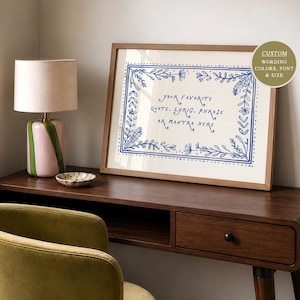 May include: A framed rectangular print featuring a blue hand-drawn floral border and the text "YOUR FAVORITE QUOTE, LYRIC, PHRASE OR MANTRA HERE" in blue ink on a cream background. A circular badge in the top right corner reads "CUSTOM WORDING COLORS, FONT & SIZE".