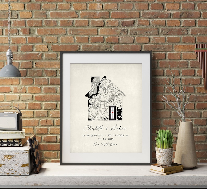 May include: Black and white print of a house-shaped map with a red door. The text "Charlotte & Andrew" is written below the map, along with coordinates and the date "12-18-2019". The text "Our First Home" is written below the date.