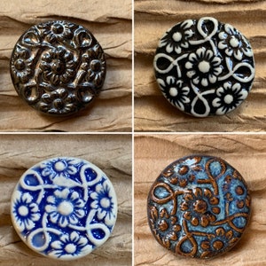Könnte beinhalten: Vier Keramikknöpfe mit floralem Design. Die Knöpfe sind in verschiedenen Farben, darunter Schwarz, Weiß, Blau und Braun.