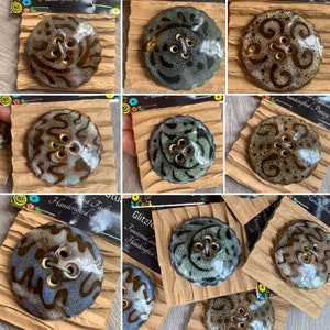 May include: A collection of handcrafted pottery buttons in various colors and patterns. Each button is round with four holes and a decorative design. The buttons are displayed on brown paper.