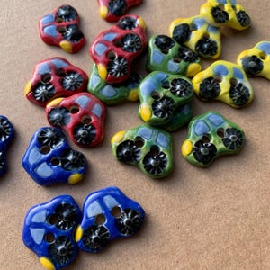 Op de afbeelding: Assortiment van keramische knopen in de vorm van auto's in rood, groen, blauw en geel. De knopen hebben twee gaten om te naaien.