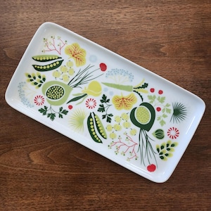 May include: A rectangular white ceramic serving tray featuring a colourful botanical pattern of green pea pods, yellow and green leaves, small red berries, and light blue floral clusters scattered across the surface in a flat graphic design style.