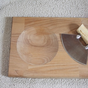May include: A wooden cutting board with a built-in bowl and a curved knife with a bone handle.
