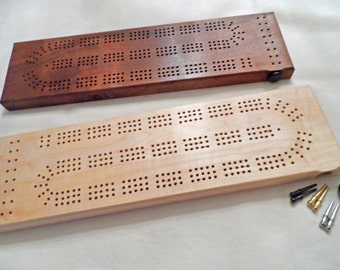 May include: Two wooden cribbage boards, one light brown and one dark brown, with pegs and a white background.
