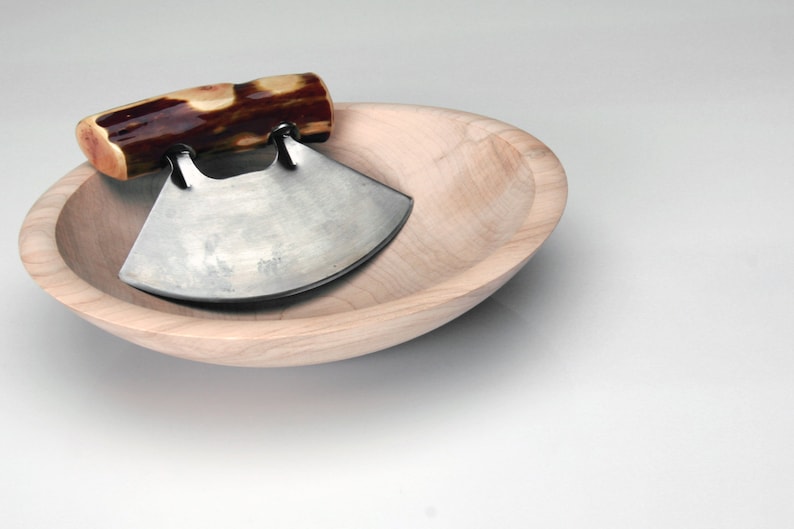 May include: A wooden bowl with a curved, stainless steel knife with a wooden handle. The knife is resting in the bowl.
