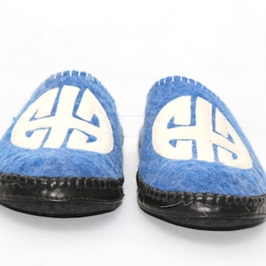 May include: A pair of blue wool slippers with a white embroidered design. The slippers have a black rubber sole.