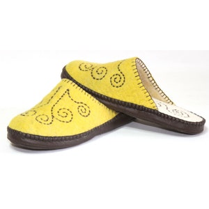 Può includere: Un paio di pantofole in feltro giallo con bordino marrone e un motivo a spirale nero.