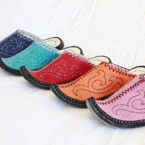 Pode incluir: Cinco pares de pantufas de feltro em diferentes cores, incluindo azul, turquesa, vermelho, laranja e rosa. Cada pantufa tem um design bordado &uacute;nico e uma sola de borracha preta.