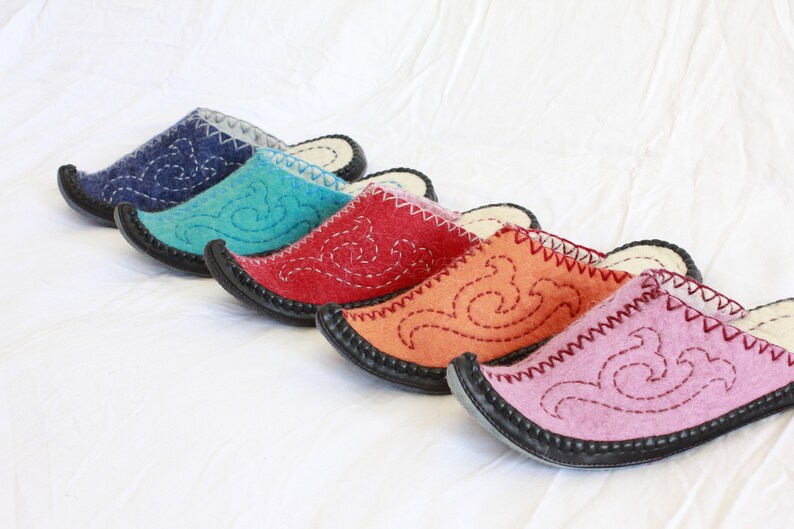 Pode incluir: Cinco pares de pantufas de feltro em diferentes cores, incluindo azul, turquesa, vermelho, laranja e rosa. Cada pantufa tem um design bordado &uacute;nico e uma sola de borracha preta.