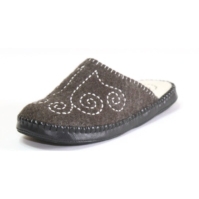 May include: Gray felt slippers with a white embroidered design. The slippers have a black leather trim around the sole.