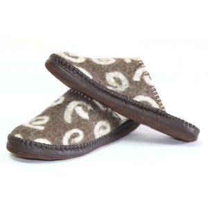 May include: A pair of brown wool slippers with a white swirl pattern. The slippers have a brown leather sole and a stitched seam around the edge.