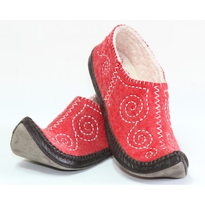 May include: A pair of red felt slippers with white stitching in a swirling pattern. The slippers have a brown leather trim and a pointed toe.