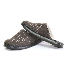 May include: A pair of brown felt slippers with white embroidered swirls. The slippers have a black leather trim and a closed toe.