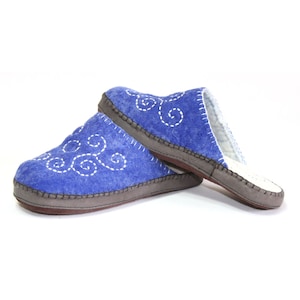 May include: A pair of blue felt slippers with white embroidered swirls. The slippers have a brown leather sole and a white fleece lining.