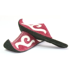 May include: A pair of red felt slippers with white embroidered designs. The slippers have black soles and are folded over each other.