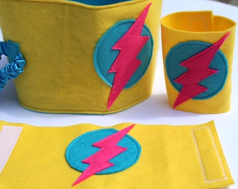 May include: Yellow felt superhero arm bands with a turquoise and pink lightning bolt design. The arm bands are perfect for a child's costume.