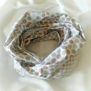 May include: A white infinity scarf with a brown and grey polka dot pattern on one side and a brown and white plaid pattern on the other side.