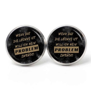 May include: Two round black and silver cufflinks with a white galaxy background. The cufflinks have gold text that reads "WENN DAS DIE LÖSUNG IST WILL ICH MEIN PROBLEM ZURÜCK!"