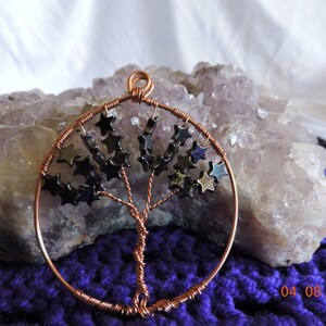 May include: A copper wire tree of life pendant with black star-shaped beads. The pendant is resting on a large amethyst crystal.