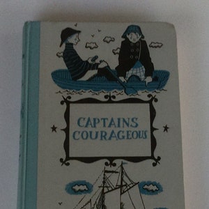 May include: A vintage book cover with a blue and white color scheme. The cover features an illustration of two boys in a boat, a sailboat, and the title "CAPTAINS COURAGEOUS".